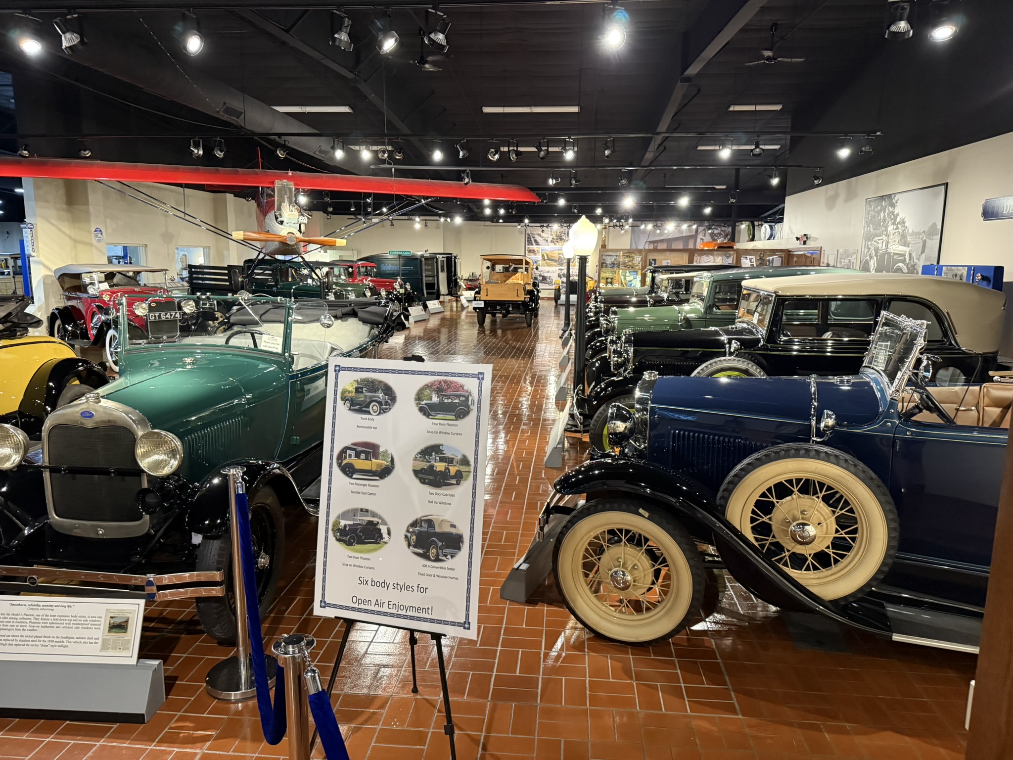 Model A Ford Museum gallery at Gilmore, with body-style sign and biplane overhead